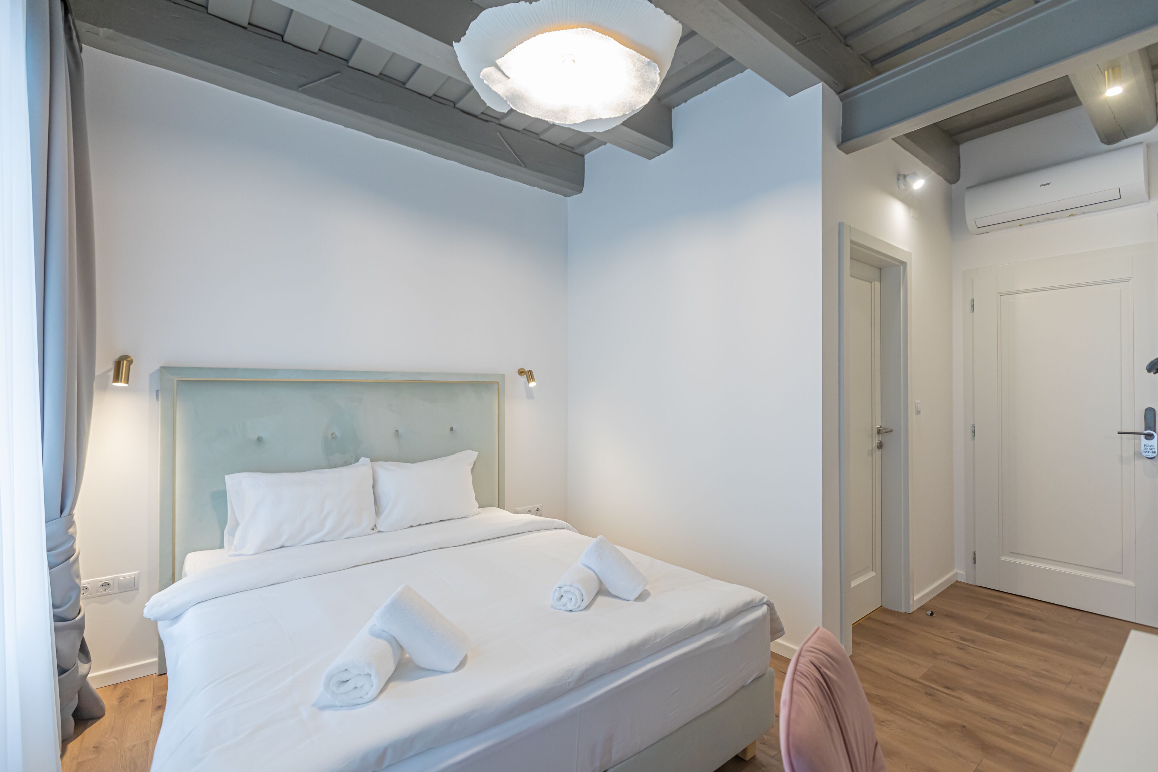 A neatly made bed with white linens and towels, a light blue headboard, and a modern pendant light fixture.