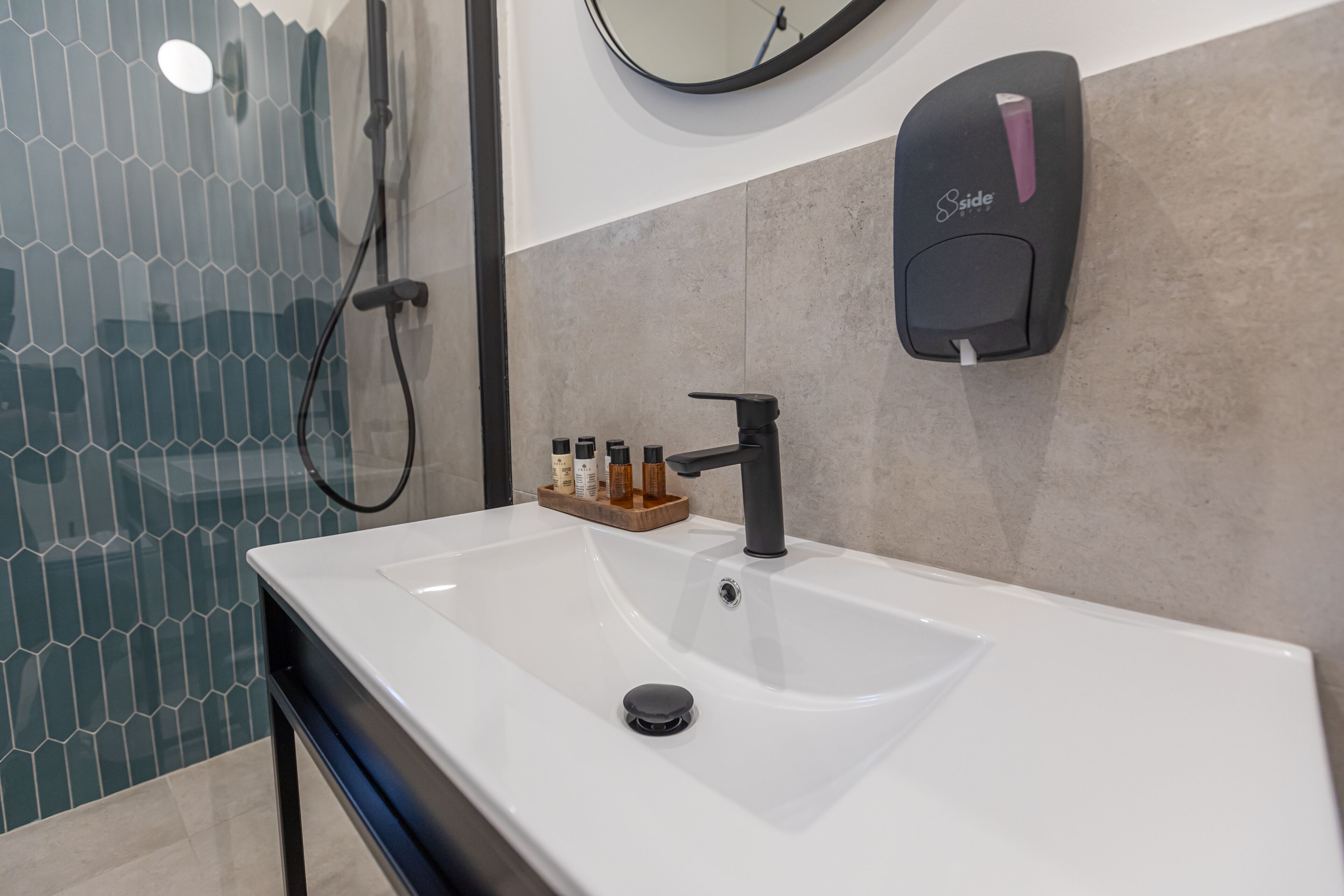 Une salle de bain moderne avec un lavabo blanc, un robinet noir et un distributeur de savon fixé au mur.