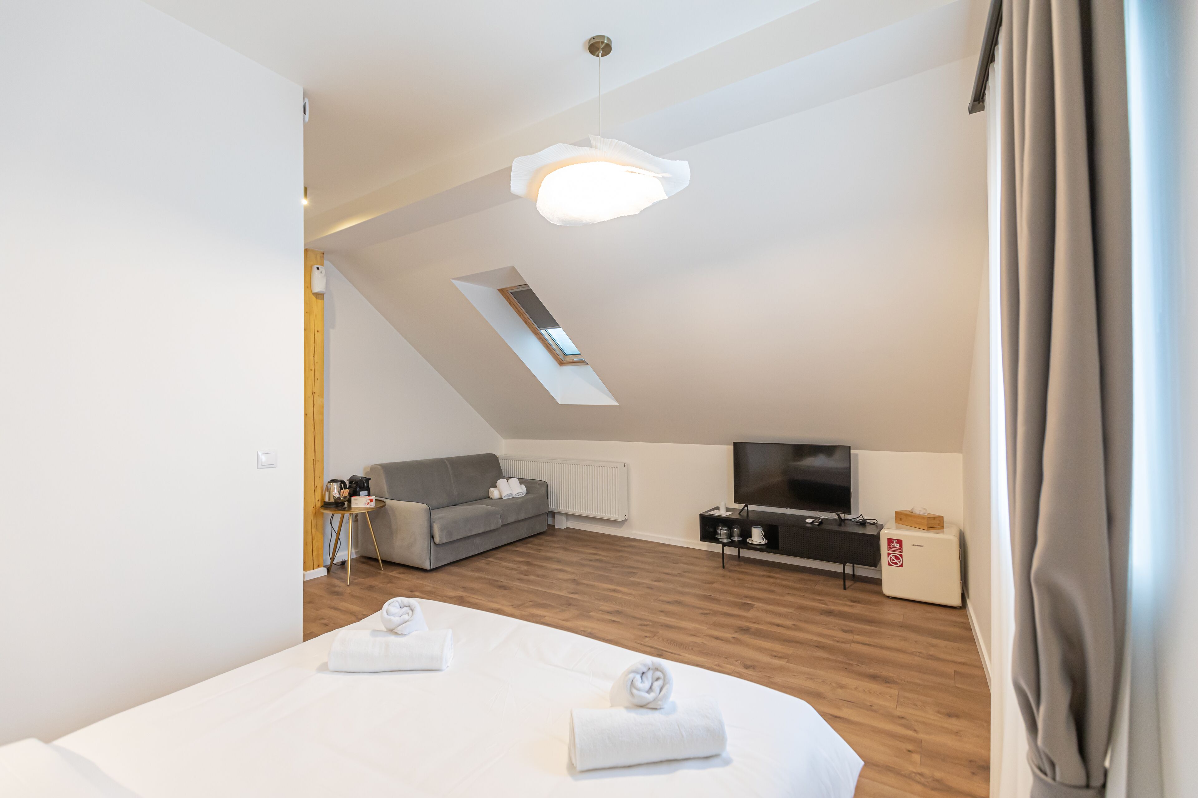 Une chambre d’hôtel moderne avec un plafond de style industriel, un téléviseur à écran plat, un canapé et un lit avec des serviettes.