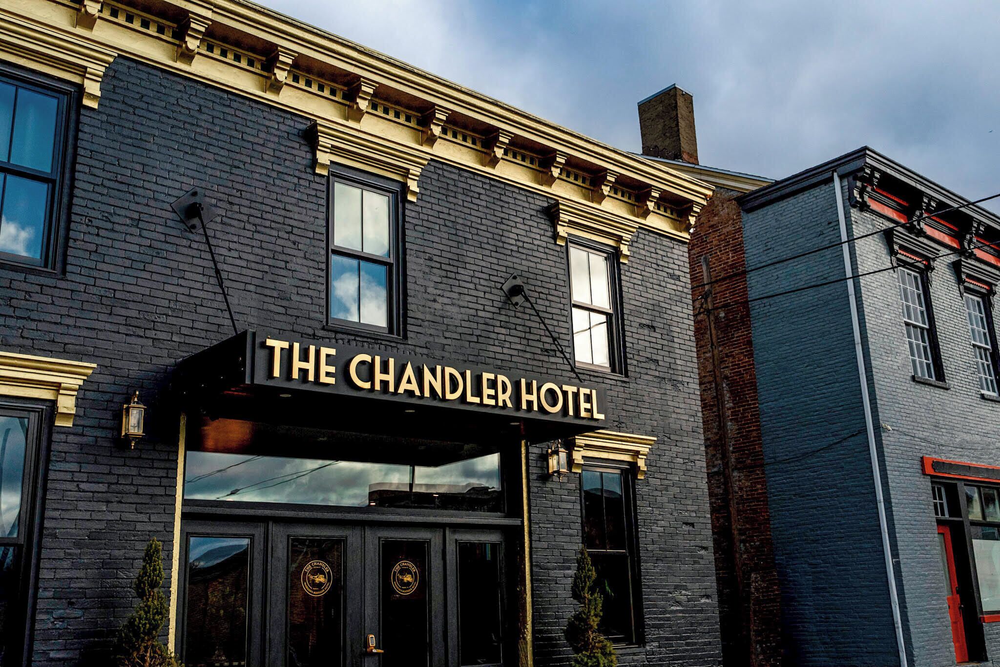 The exterior of The Chandler Hotel with a black facade, gold trim, and a prominent sign.