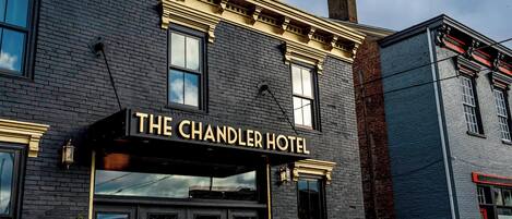 The exterior of The Chandler Hotel with a black facade, gold trim, and a prominent sign.