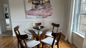 Ruokailutilassa on lasipöytä ja puutuolit, moderni kattokruunu sekä suuri, abstrakti taulu seinällä.
