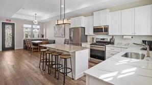 A modern kitchen with white cabinets, a central island with stools, stainless steel appliances, and a pendant light. - The Hudson: Dog Friendly, Private Hot Tub, Community Pool + Hot Tub (Hurricane)