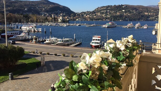 A harbor with boats, a pedestrian walkway, and a mountainous backdrop.