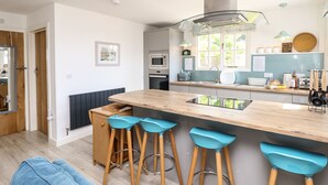 A modern kitchen with a central island, bar stools, and a view of the adjacent dining area. - The Stables (Newport)