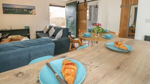 A cozy living room with a sofa, dining table with blue plates and a croissant, and a chandelier. - The Stables (Newport)