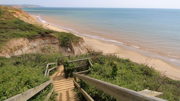 A wooden staircase leading to a beach with a clear view of the ocean. - The Stables (Newport)