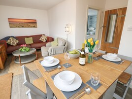 Un comedor con una mesa de madera dispuesta para cuatro, un sofá rojo, una mesita redonda con una planta y un cuadro en la pared.
