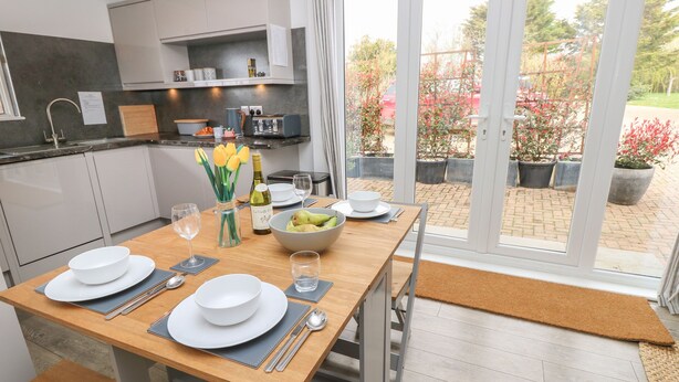 Una cocina moderna con comedor, que presenta una mesa de madera preparada para dos personas, un jarrón con tulipanes amarillos y un frutero.