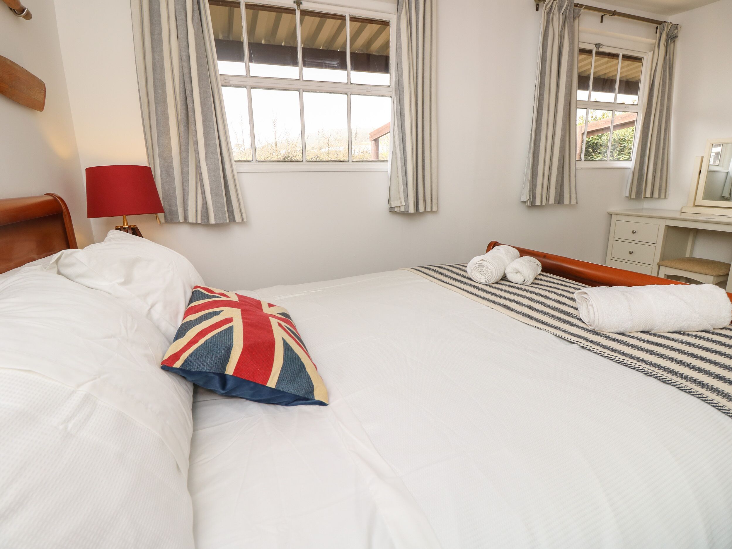 Habitación de hotel con cama, mesita de noche, lámpara, ventana con cortinas y cómoda.