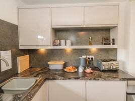 Una cocina moderna con armarios blancos, encimera de mármol, un lavabo, un tostador y una cafetera.