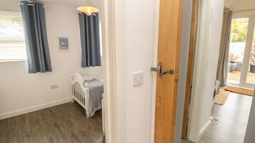 Een kamer met een houten vloer, een witte deur, een babybedje en een raam met blauwe gordijnen.