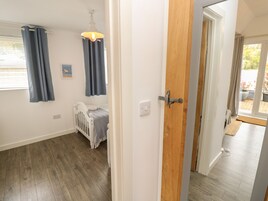A room with a wooden floor, a white door, a baby crib, and a window with blue curtains.