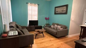 A living room with a teal wall, a grey sofa, a television, and a wooden floor.