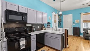 A kitchen with grey cabinets, a black stove, and a white countertop.