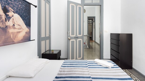 Habitación de hotel con una cama, un tapete a rayas, un cuadro en la pared y una puerta que da a otra habitación.