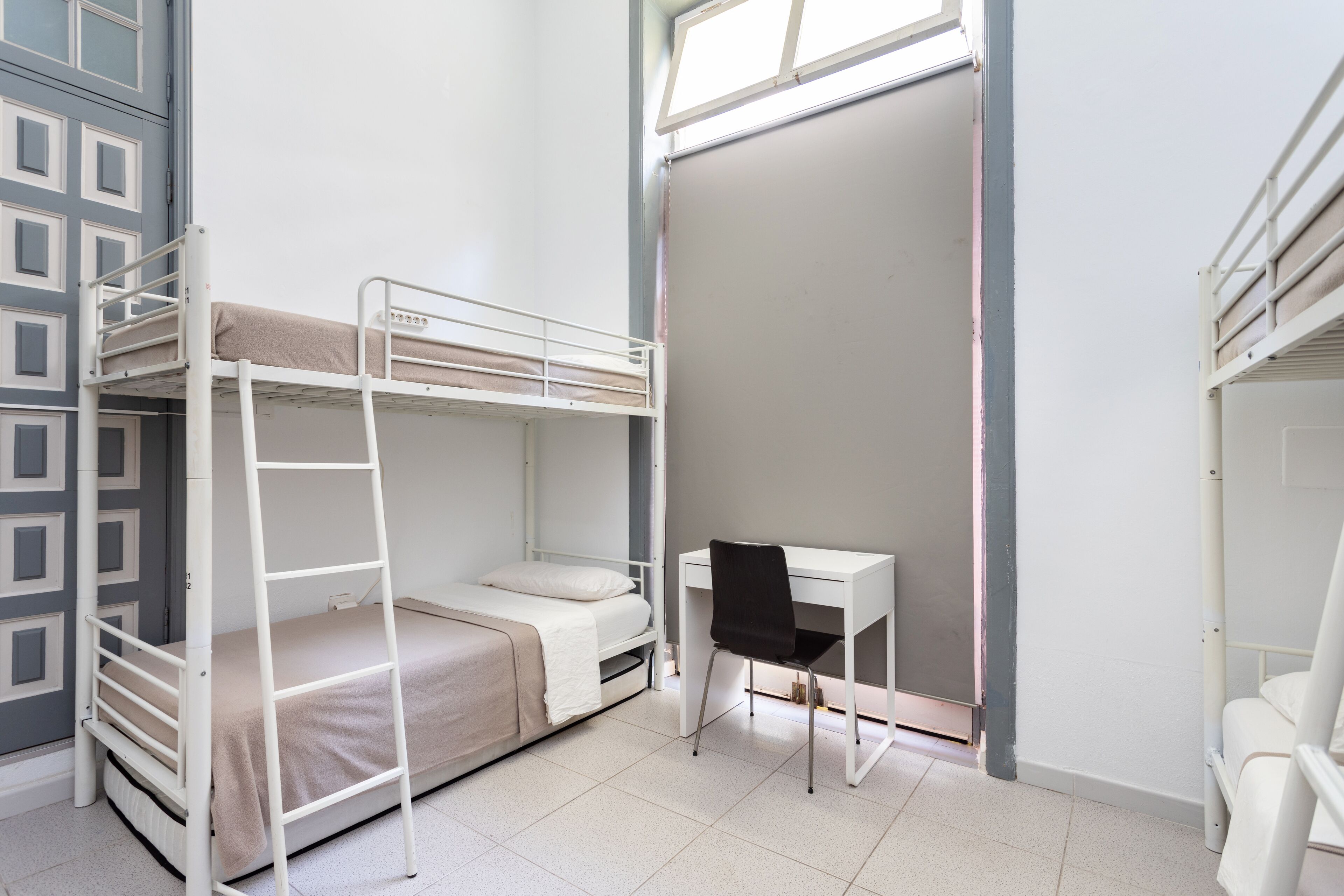 A dormitory room with bunk beds, a desk, and a chair.