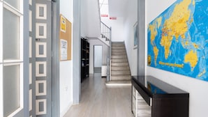 Un pasillo con suelo de madera, una escalera, un mapa en la pared y una puerta con un letrero.