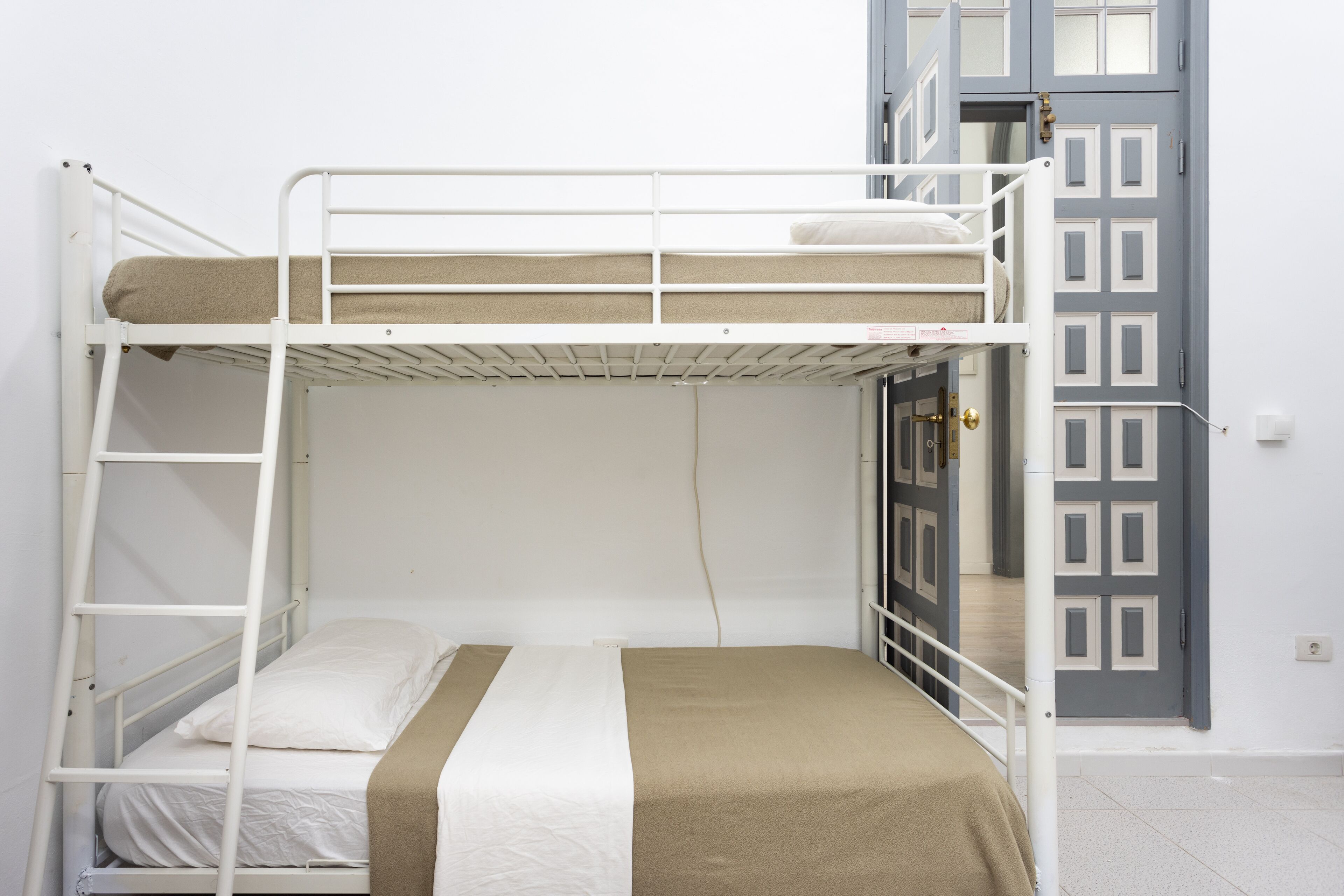 A bunk bed with a ladder, a single bed below, and a door with a geometric pattern.