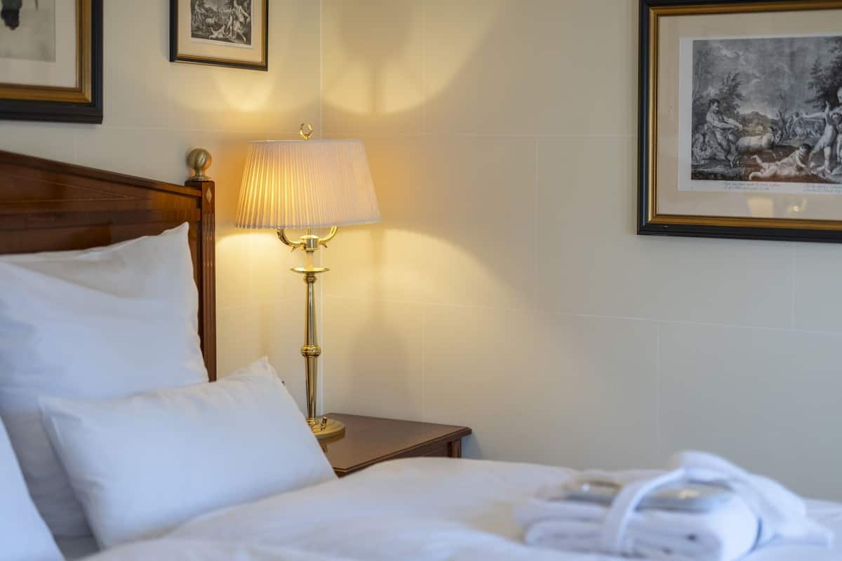 A hotel room with a neatly made bed, a bedside lamp, and framed artwork on the walls.