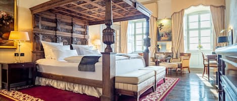 A four-poster bed with a red and gold patterned rug, wooden furniture, and a large window with curtains.