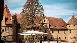 A courtyard with stone flooring, outdoor seating, and a large tree.