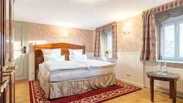 A neatly made bed with a wooden headboard, a red and gold patterned rug, and a window with curtains.