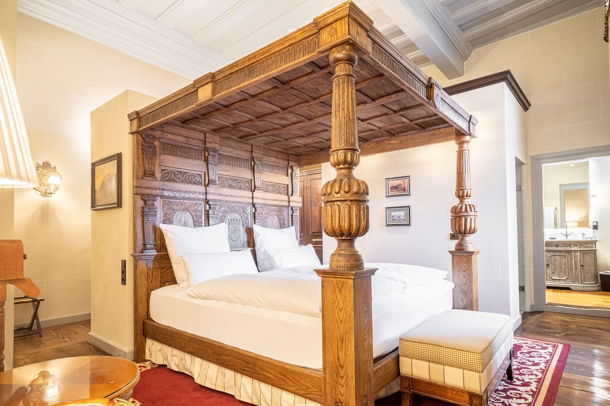 A four-poster bed with a wooden headboard, a red carpet, and a wooden bench beside it.