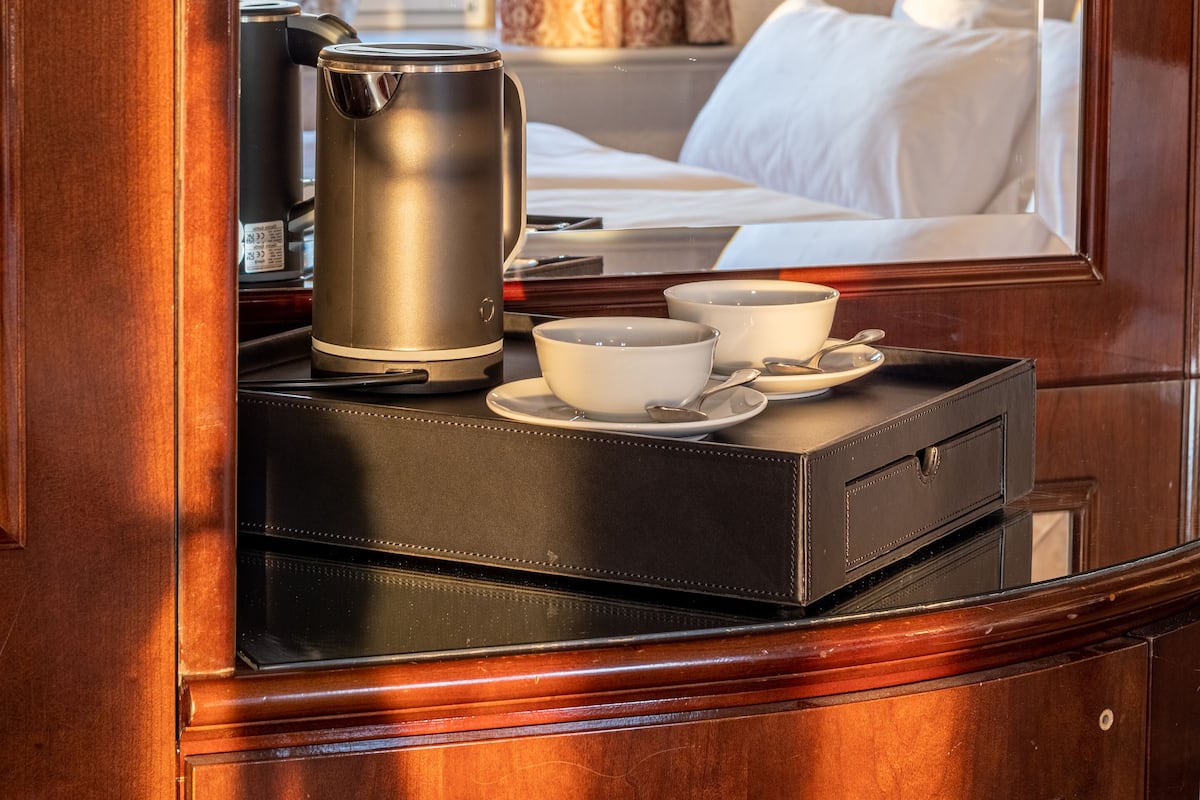 A hotel room with a wooden desk, a kettle, a cup, and a tray.