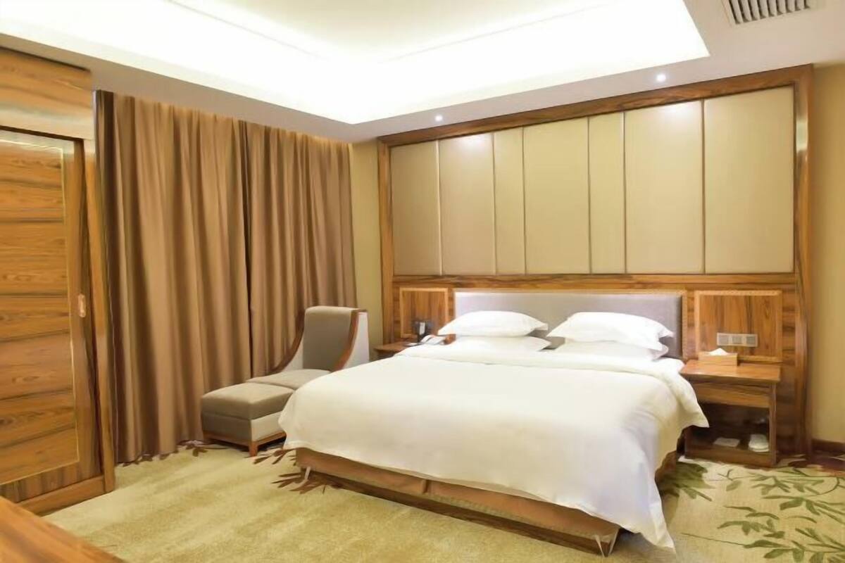 Une chambre d’hôtel avec un lit, une chaise, une table de chevet et une armoire en bois.