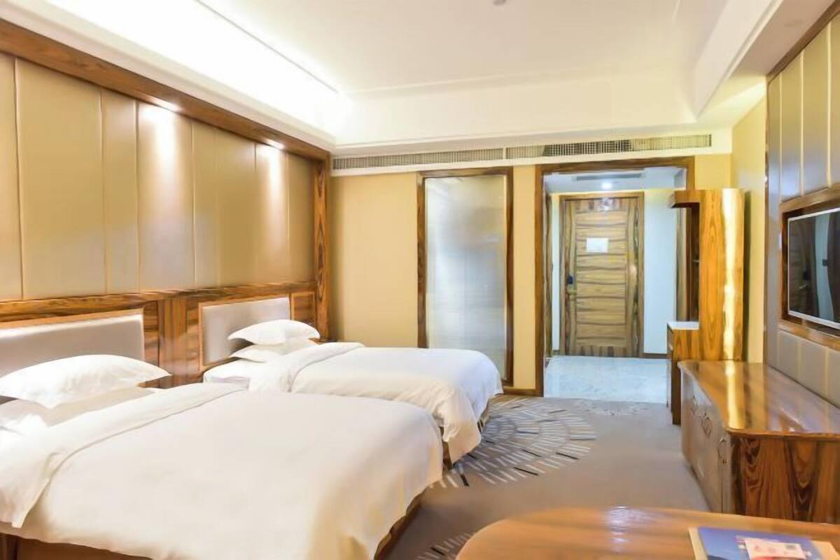 Une chambre d’hôtel avec deux lits, une télévision, une commode en bois et un dressing.