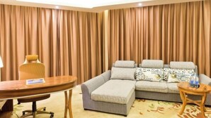 Een hotelkamer met een bank, een klein rond tafeltje, een stoel en een groot raam met gordijnen.