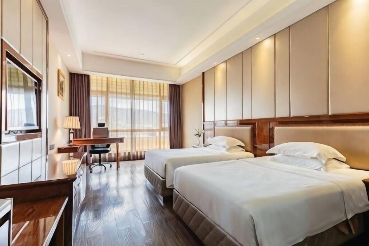 Une chambre d’hôtel avec deux lits, un bureau, une chaise et une grande fenêtre.