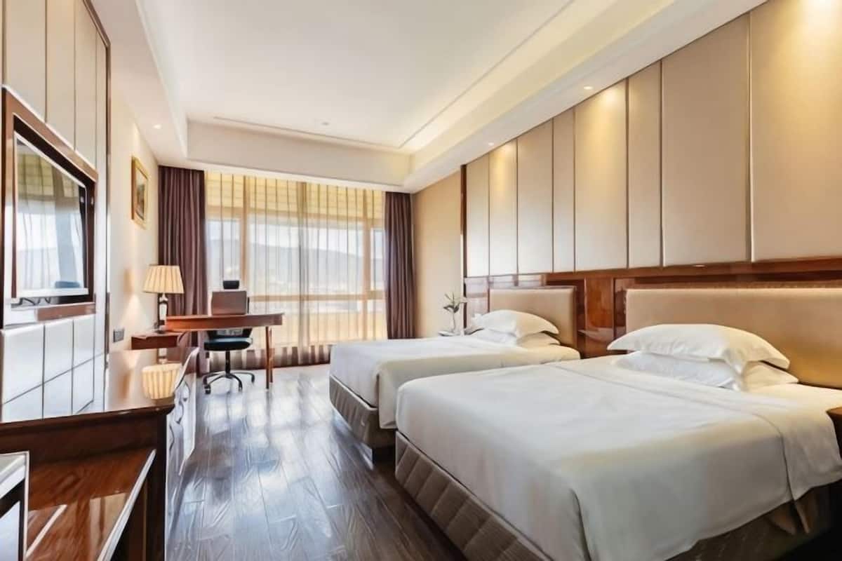 A hotel room with two beds, a desk, a chair, and a large window.