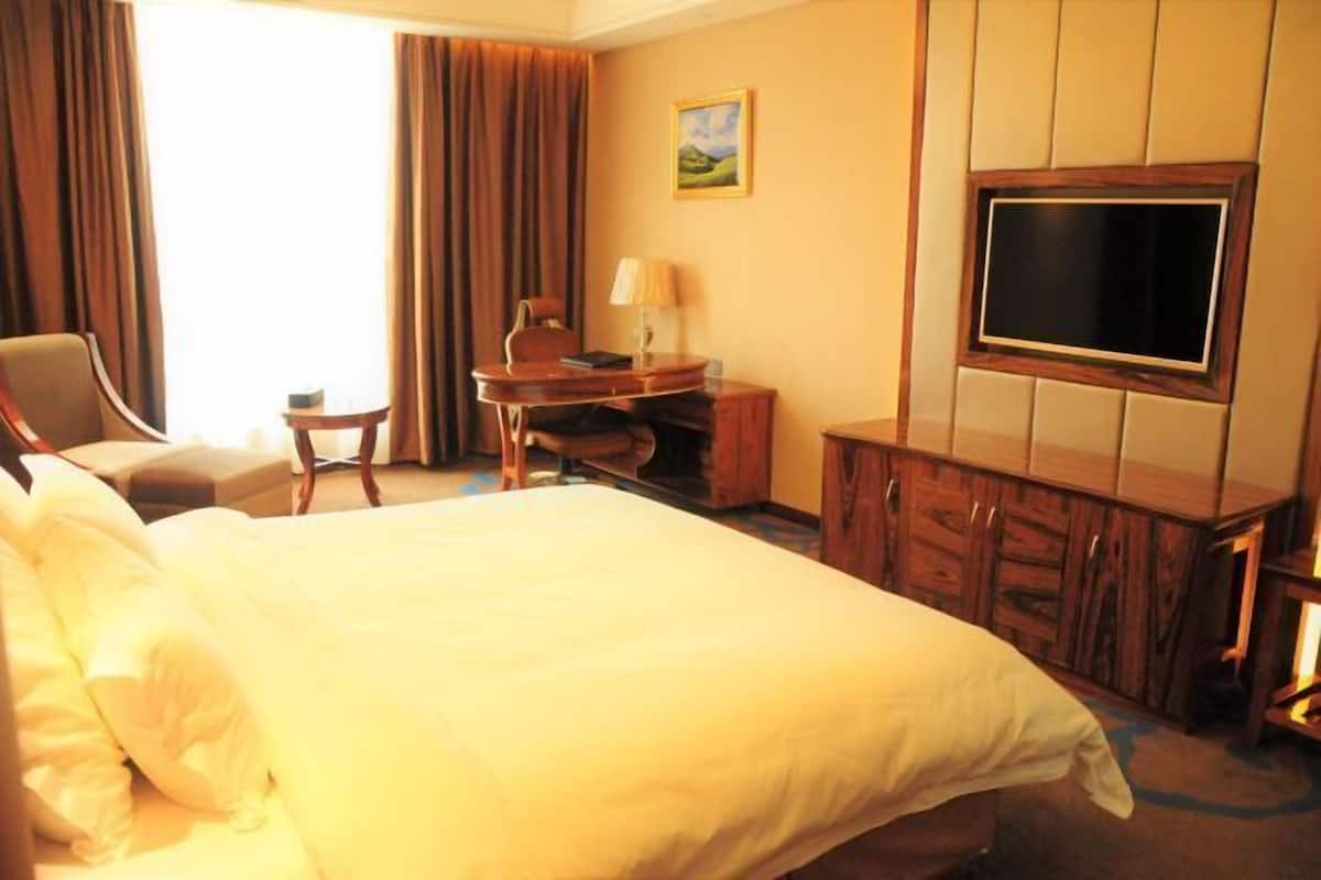 Une chambre d’hôtel avec un grand lit, un bureau, une chaise, une télévision et un tableau au mur.