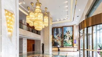 A hotel lobby with a large chandelier, a reception desk, and a mural on the wall.