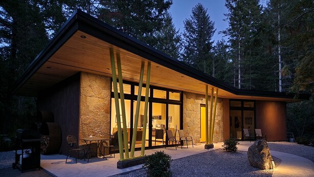 Una casa moderna con fachada de piedra, amplios ventanales y un patio bien iluminado.