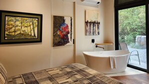 Un baño moderno con una bañera independiente, techo de madera y obras de arte en las paredes.