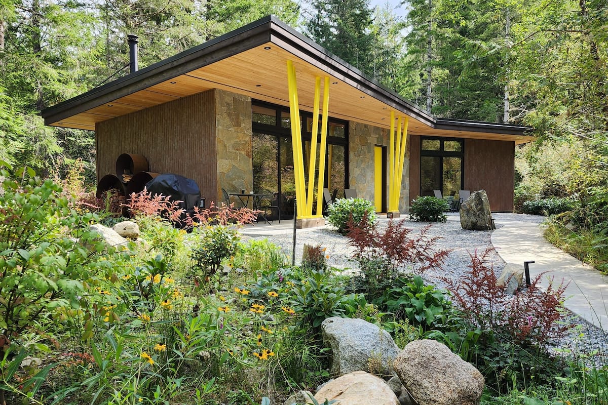 A modern building with a wooden exterior and large windows, surrounded by a garden with various plants and rocks.