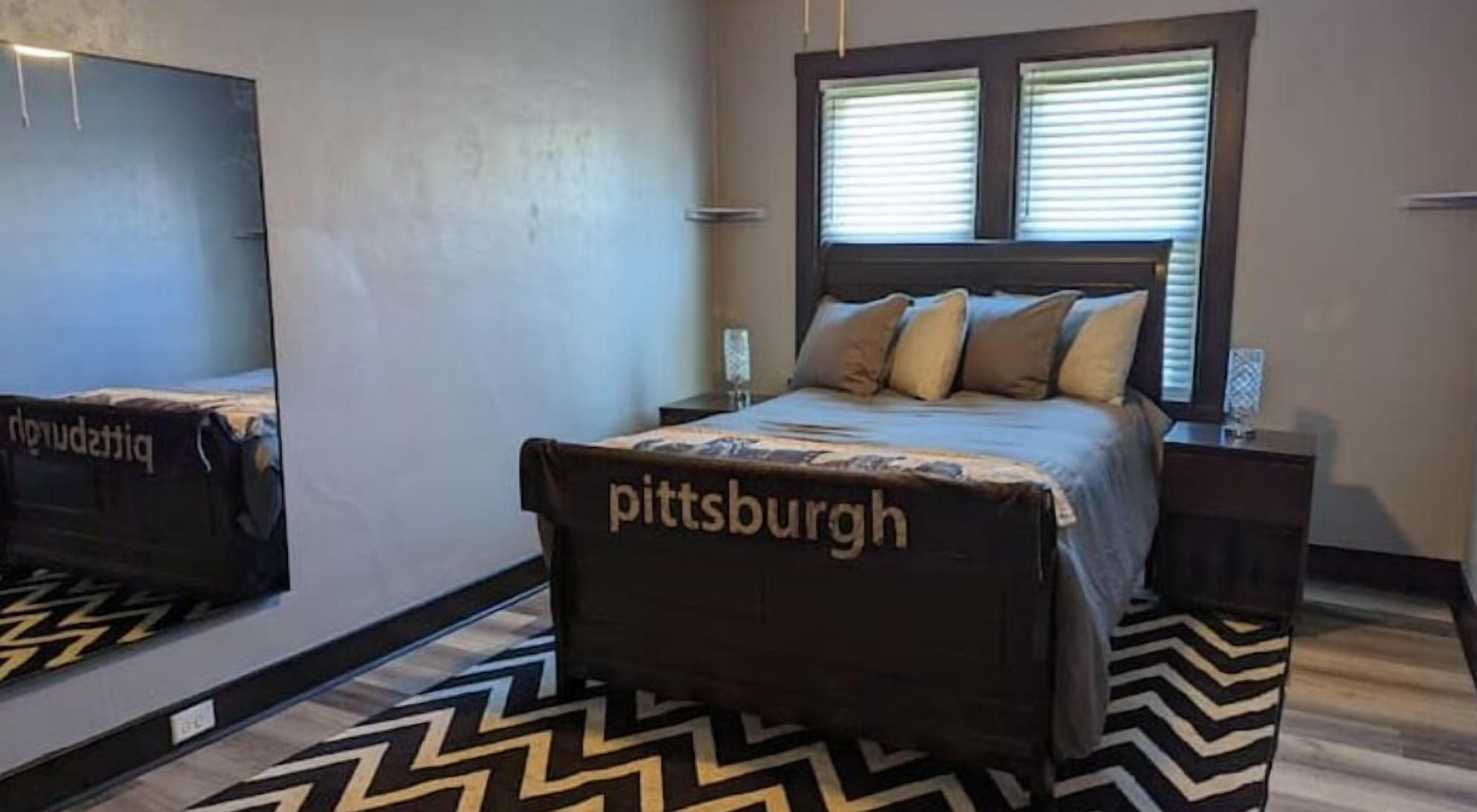 Ein Schlafzimmer mit einem Bett, einem Nachttisch, einem Spiegel und einem Fenster mit Jalousien.