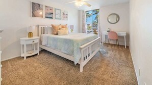 Une chambre à coucher comprenant un lit, un bureau, une chaise, un ventilateur de plafond et une fenêtre donnant sur un beau paysage.