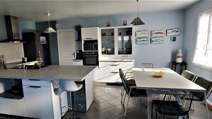 Una cucina moderna con isola centrale, un'area pranzo con tavolo e sedie, e vista sullo spazio abitativo adiacente.