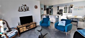 Een moderne woonkamer met een televisie, blauwe fauteuils en een glazen salontafel.