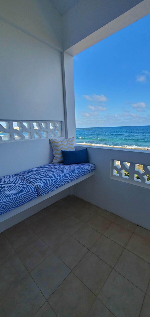Un balcón con un sofá azul estampado, una almohada amarilla y azul, y vista al océano.