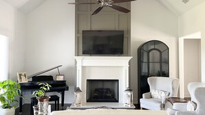 A spacious living room with a fireplace, a piano, and a ceiling fan. - Visit Auburn in Style: Luxurious House on Golf Course, Perfect for Families (Auburn)
