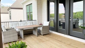 A covered outdoor patio with a wooden deck, wicker furniture, and a glass door leading to a balcony. - Visit Auburn in Style: Luxurious House on Golf Course, Perfect for Families (Auburn)