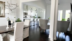 A spacious dining area with a dark wood floor, white upholstered chairs, and a central table. - Visit Auburn in Style: Luxurious House on Golf Course, Perfect for Families (Auburn)