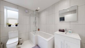 Clean lines and natural touches define this bathroom, featuring a toilet, shower, bathtub, and vanity with a mirror.