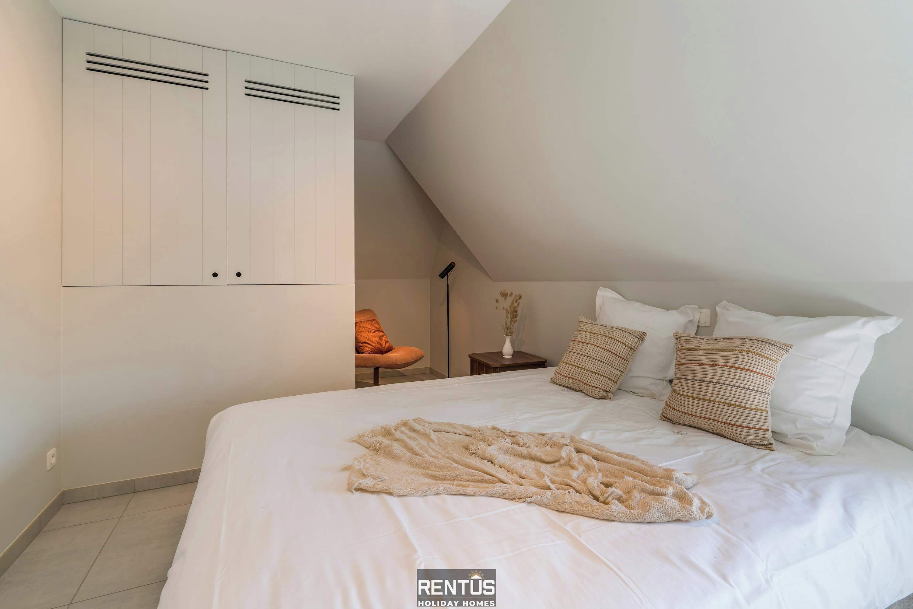 A bedroom with a large bed, a wardrobe, and a small table with a vase.