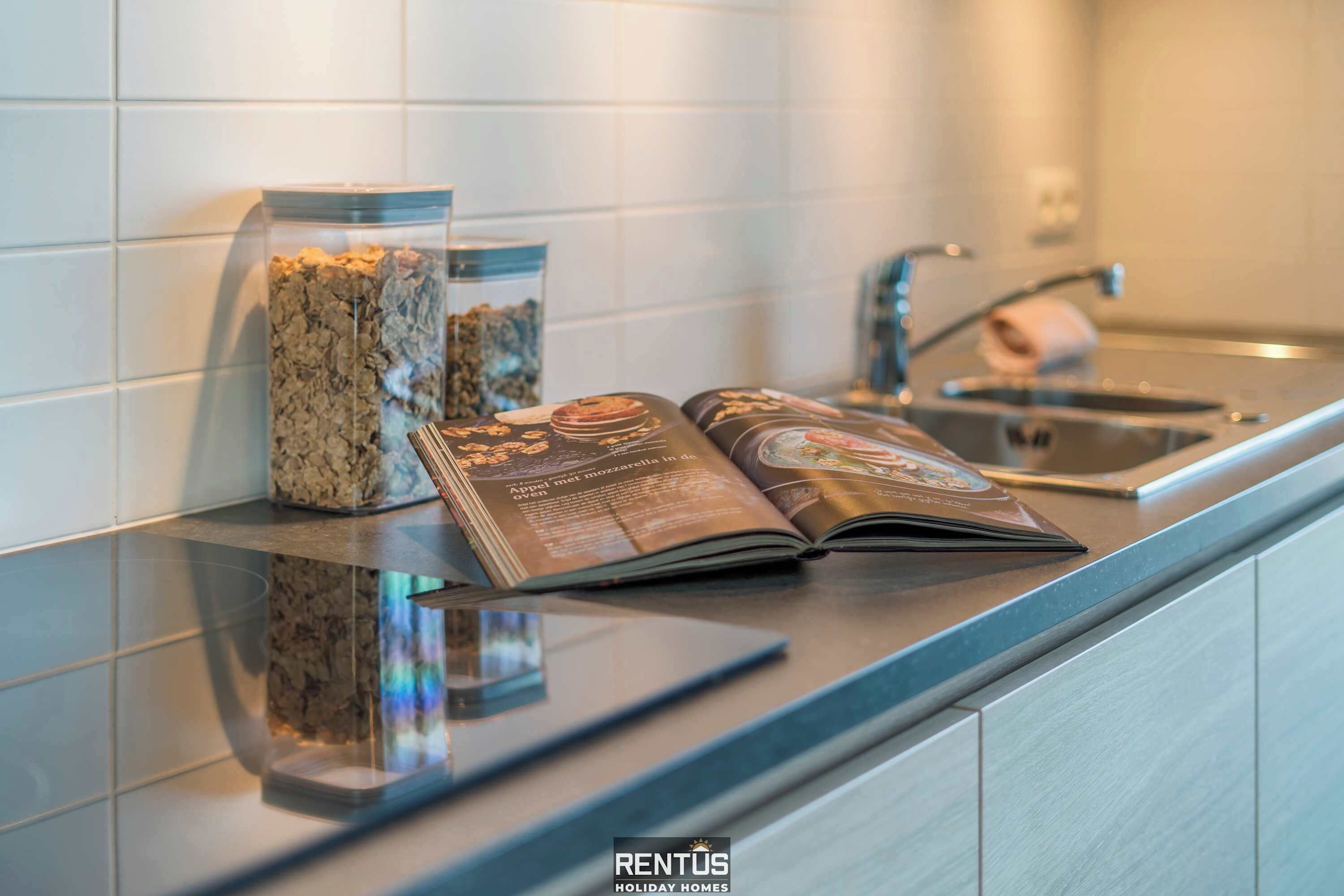 Un piano di lavoro in cucina con una rivista, un barattolo di vetro e un lavello in acciaio inossidabile.